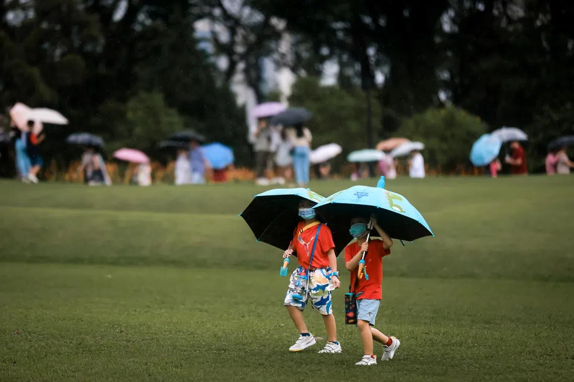 Children using umbrellas to shelter themselves at the Istana Open House, Jan 23, 2023.