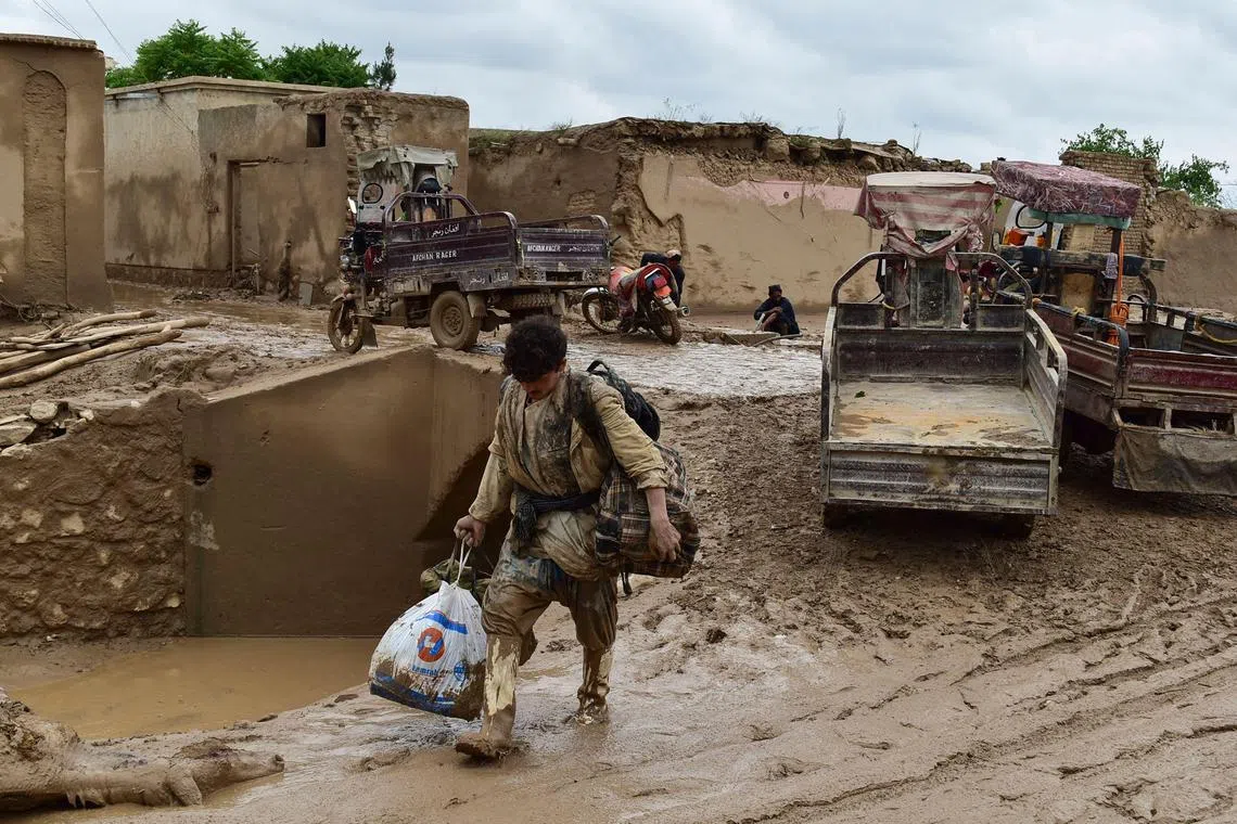 An Afghan man carries his belongings as he walks through a mud covered street following a flash flood in Laqiha village of Baghlan-i-Markazi district in Baghlan province on May 11, 2024. 