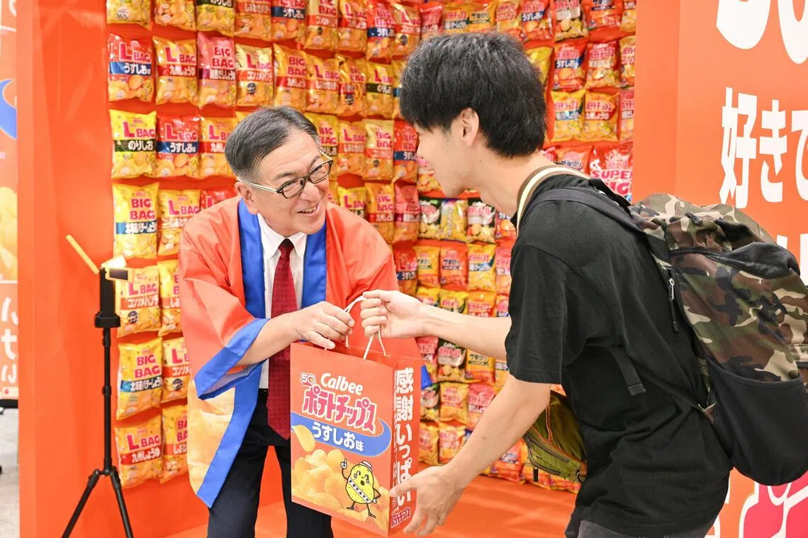 A passer-by receives a bag of Calbee potato chips from Calbee Group chief executive officer Makoto Ehara, at an event held at Tokyo Station on Sept 1 to commemorate the brand's 50th anniversary of potato chips.