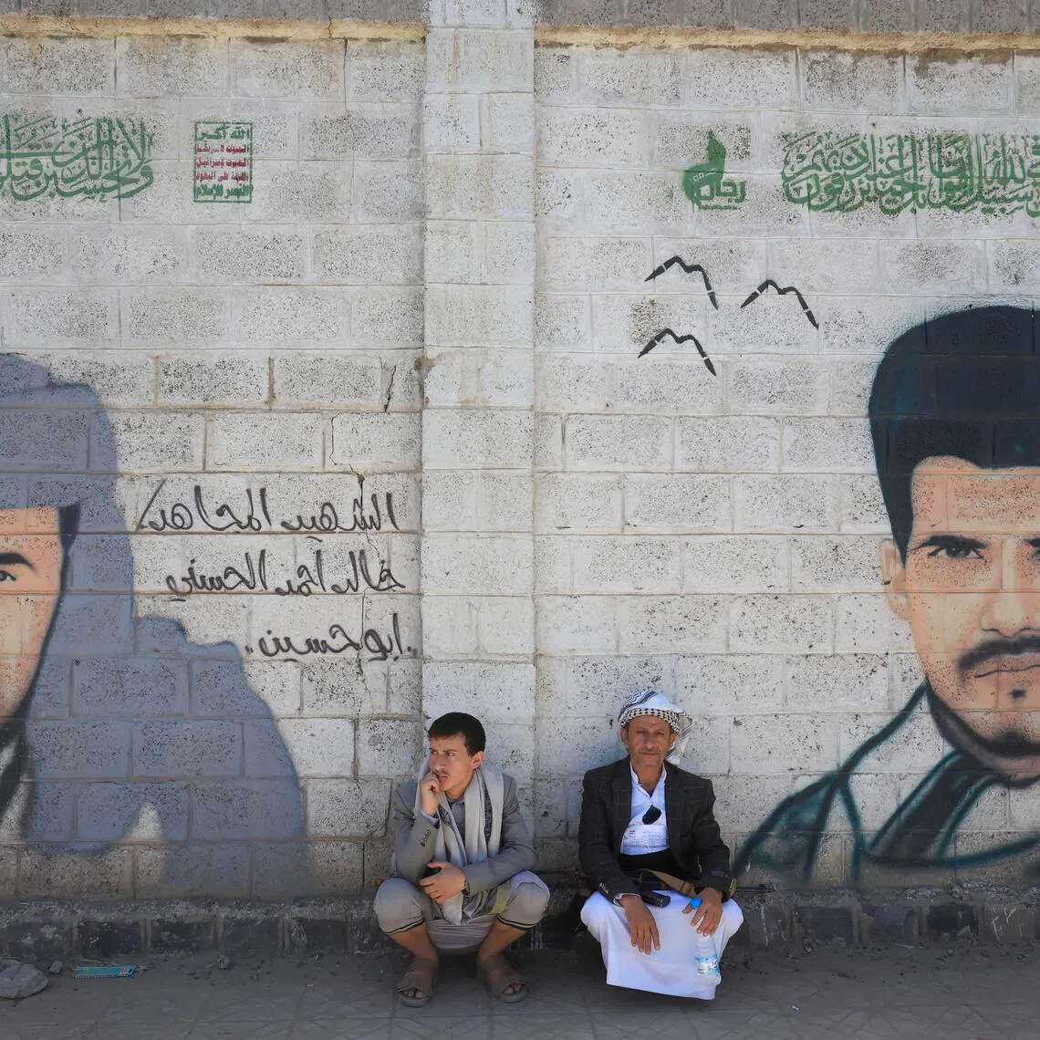 People sitting next to murals depicting portraits of slain Houthi fighters in Sana'a, Yemen, on June 4. The Houthi's threat comes as the Hormuz Strait remains blockaded by Iran.