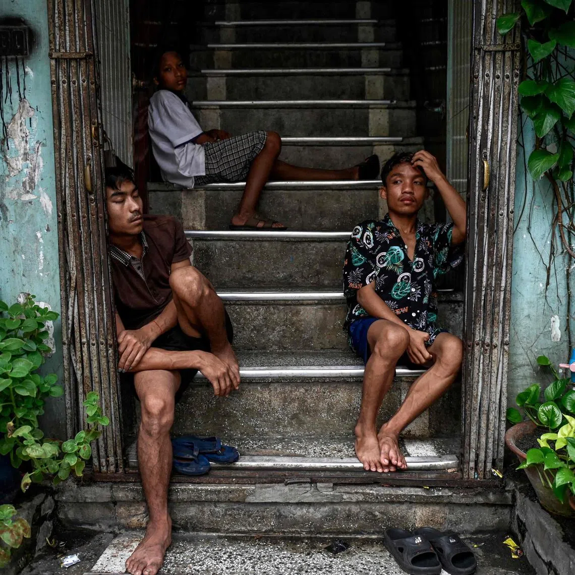 TOPSHOT - People take shelter from the rain on a building staircase in Yangon on August 19, 2025. (Photo by Sai Aung MAIN / AFP)