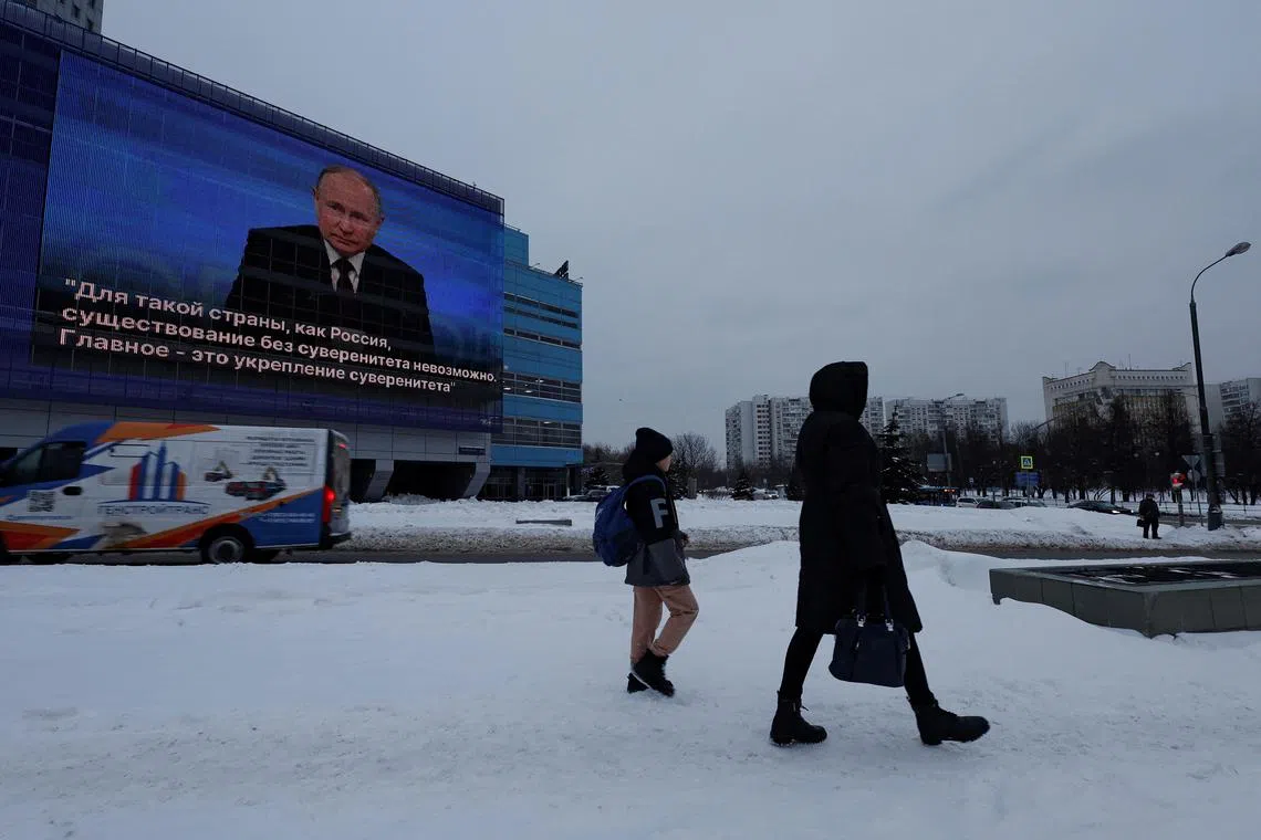 People walk past an electronic screen on the facade of a building showing an image of Russian President Vladimir Putin and a quote from his annual end-of-year press conference, in Moscow.