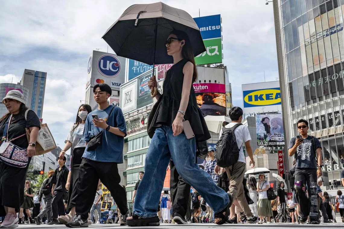 A woman uses a parasol to shelter from the sun while crossing a street in Tokyo on September 19, 2024. (Photo by Yuichi YAMAZAKI / AFP)