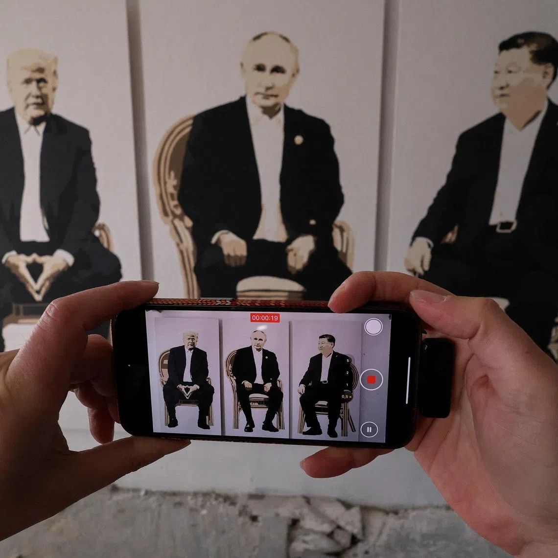 A visitor takes a video of an artwork depicting U.S. President Donald Trump, Russian President Vladimir Putin and Chinese President Xi Jinping at an exhibition, which is called \"Yalta 2.0\" and opened to make a reference to the 1945 Yalta Conference, at an art gallery in Livadia park in Yalta, Crimea, February 8, 2025. REUTERS/Alexey Pavlishak