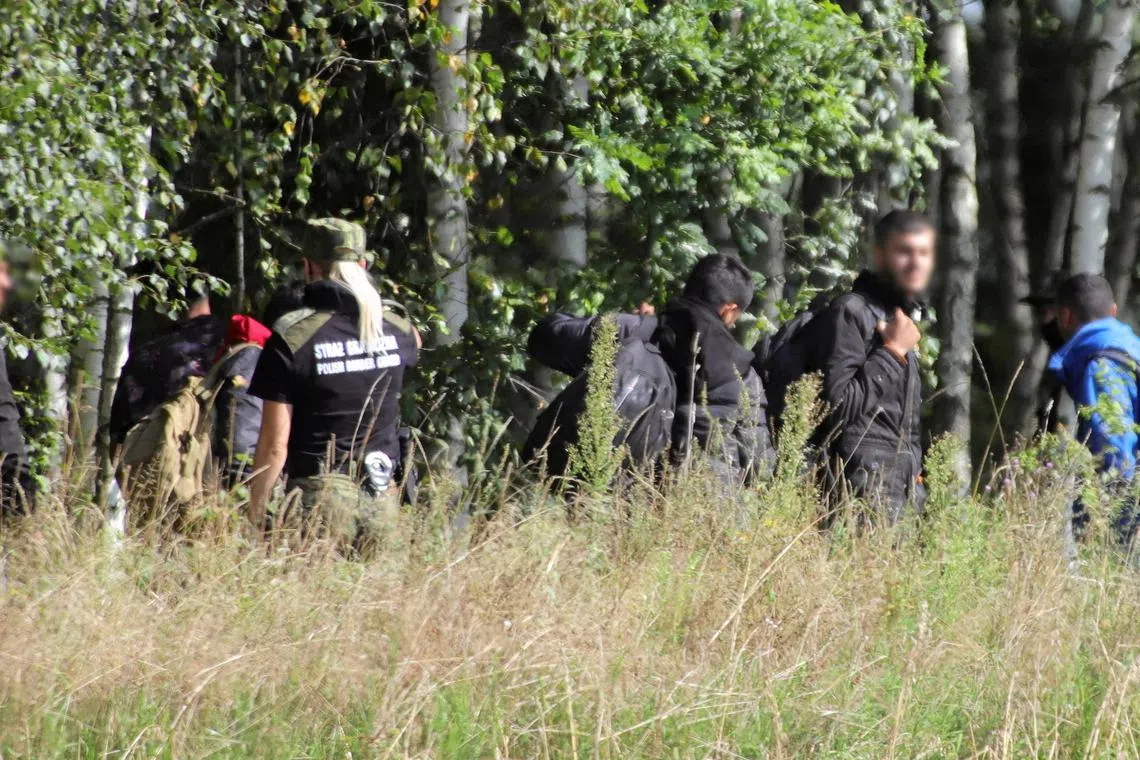 FILE PHOTO: A Polish border patrol officer is seen next to a group of migrants stranded on the border between Belarus and Poland near the village of Usnarz Gorny, Poland August 22, 2021. Grzegorz Dabrowski/Agencja Gazeta/via REUTERS/File photo