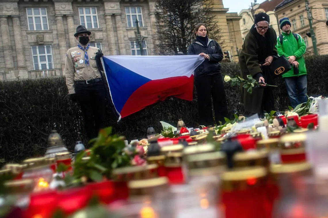 People hold the Czech national flag as they pay their respects outside the Faculty of Philosophy building at Charles University in central Prague.