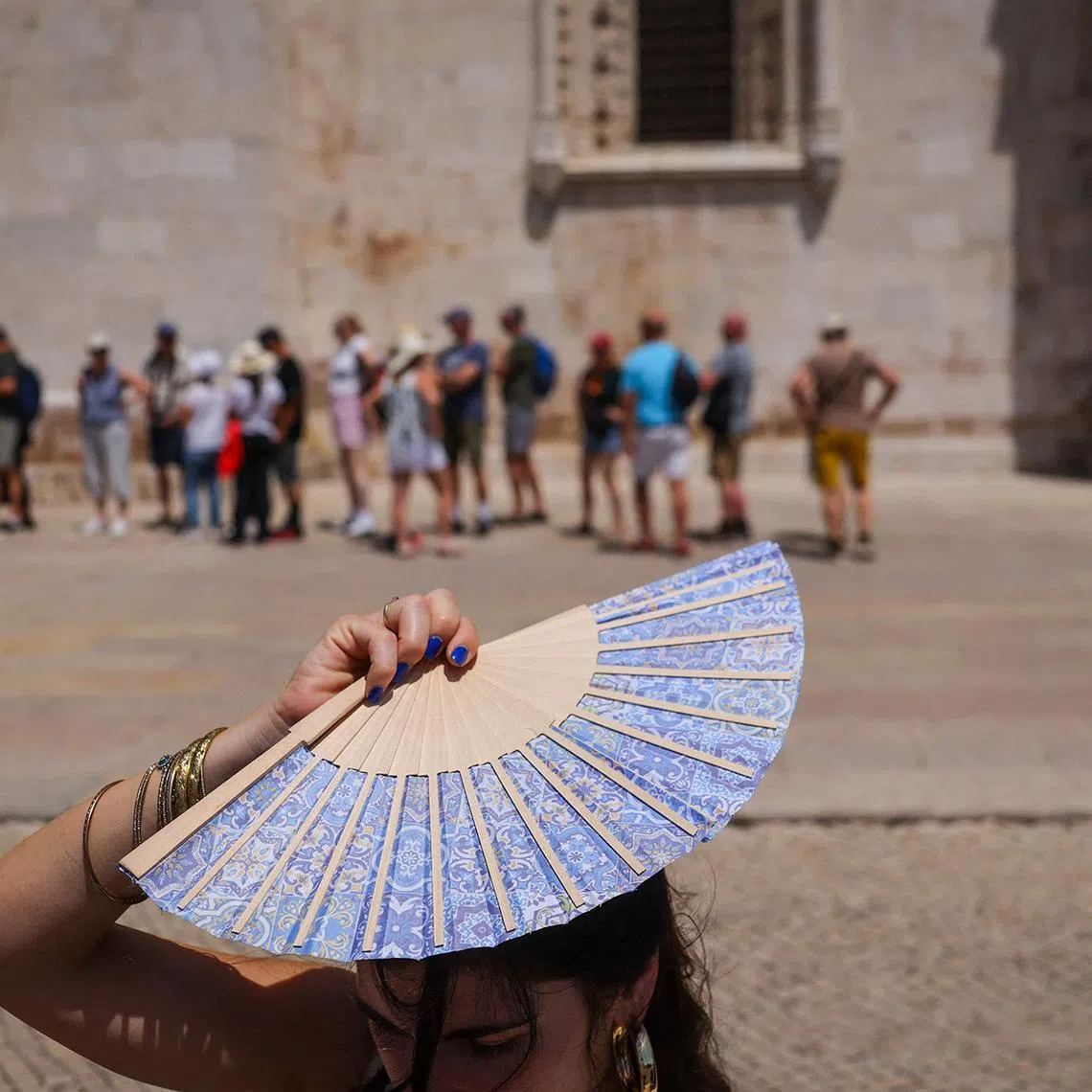 A woman shades her head with a fan in front of Jeronimos Monastery in Belem, during a heatwave in Lisbon, Portugal.