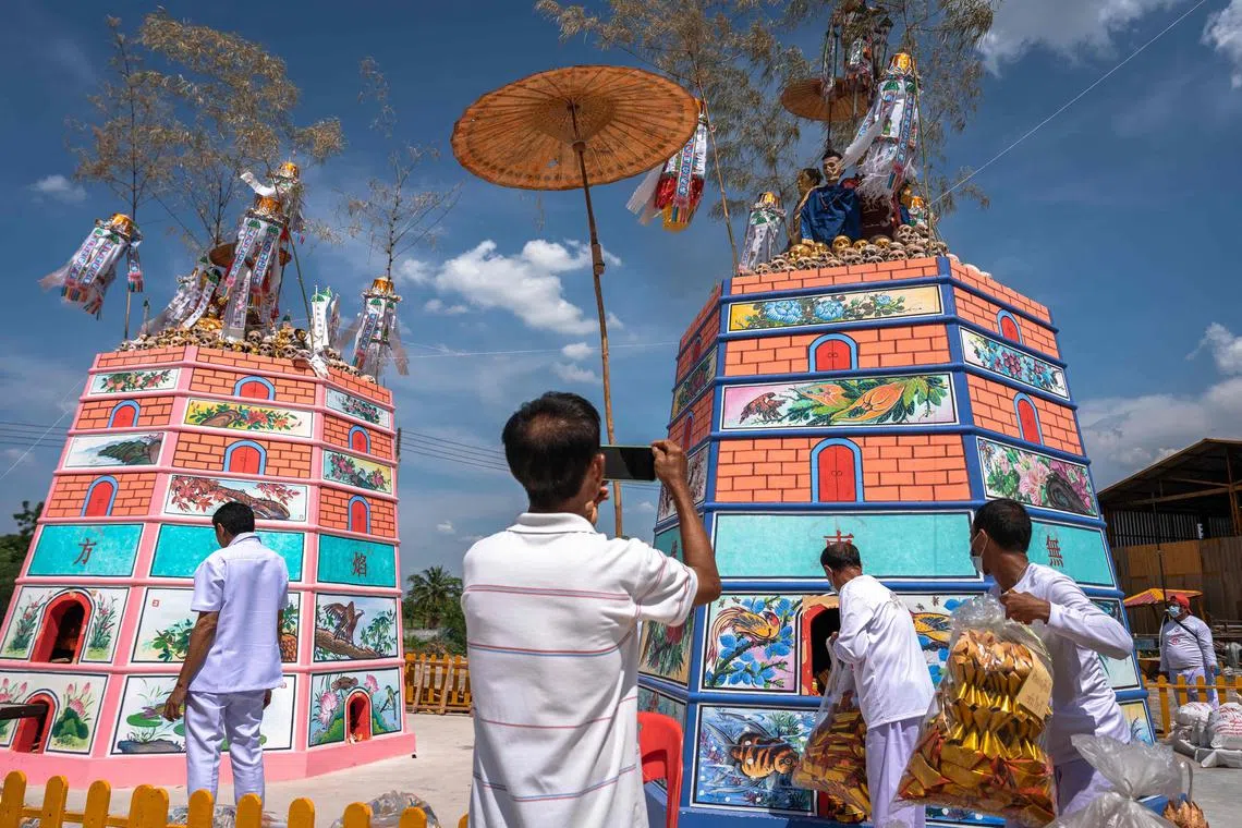 This photo taken on April 23, 2025 shows a man taking photos of mummified human remains next to skulls covered in gold leaf during the Lang Pacha ceremony at the Dhamma of Buddha Nakhon Ratchasima Foundation complex in Thailand's Nakhon Ratchasima province. Smoke rises around rows of exposed skulls as flames crackle beneath a towering crematorium in northeast Thailand -- a haunting scene that evokes a horror film but carries a sacred purpose. (Photo by Chanakarn Laosarakham / AFP) / To go with 'THAILAND-RELIGION-TRADITION,FOCUS' by Montira RUNGJIRAJITTRANON