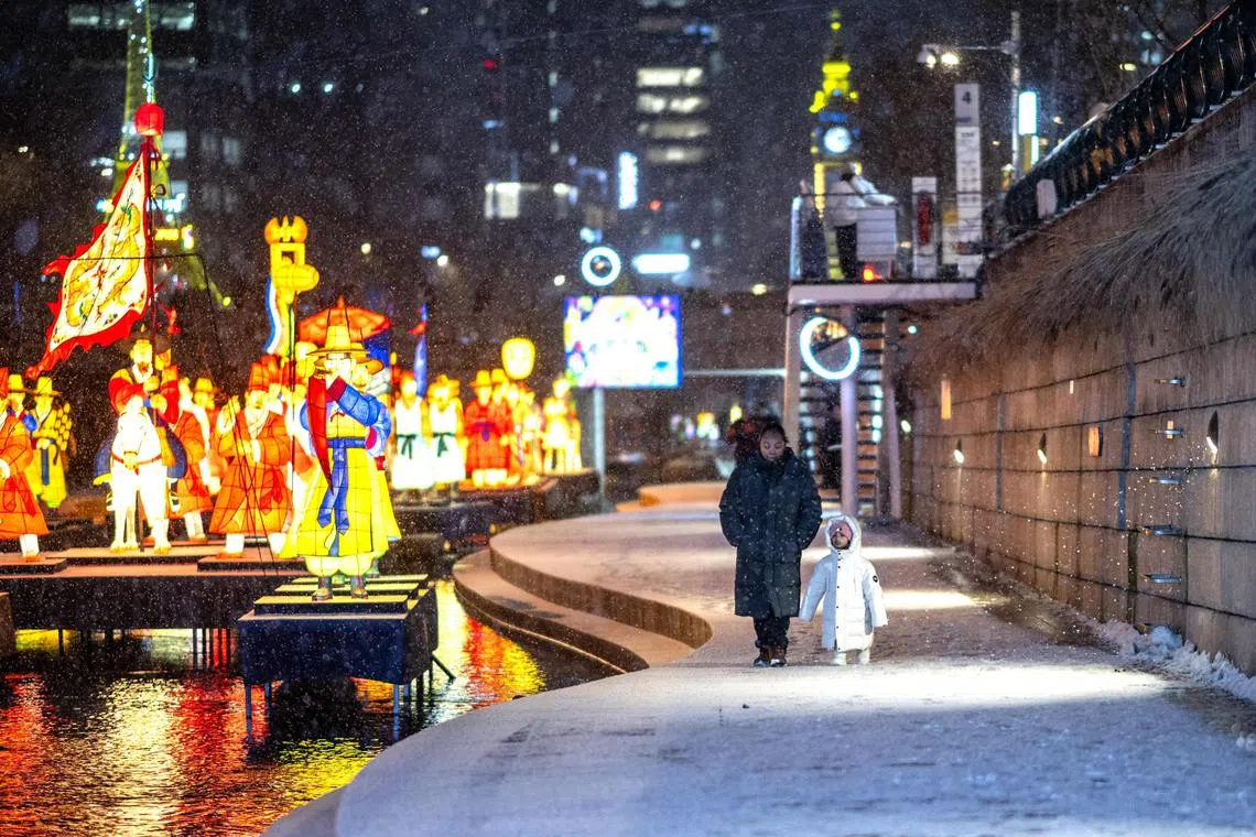 People walk along the Cheonggyecheon during snowfall in Seoul on Jan 7. In Seoul, temperatures dipped to this winter’s lowest at around minus 12 deg C.