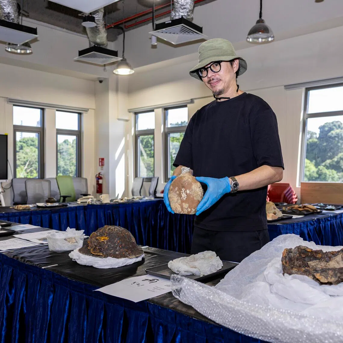 Archaeologist Aaron Kao holding a Japanese army water bottle that was found in Alexandra Hospital. On the table are British (left) and Japanese (left) helmets that were also recovered from the hospital's grounds.
