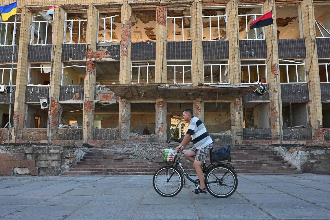TOPSHOT - A local resident rides a bicycle past a destoyed building in the town of Kupiansk, Kharkiv region on August 17, 2023, amid the Russian invasion of Ukraine. The head of the region Oleg Synegubov said that Russian forces had shelled Zaoskillya, a suburb just east of Kupiansk, killing a woman born in 1962. "Another woman, born in 1963, suffered shrapnel wounds. Medics provided assistance to the injured on the spot," he wrote on social media. (Photo by SERGEY BOBOK / AFP)