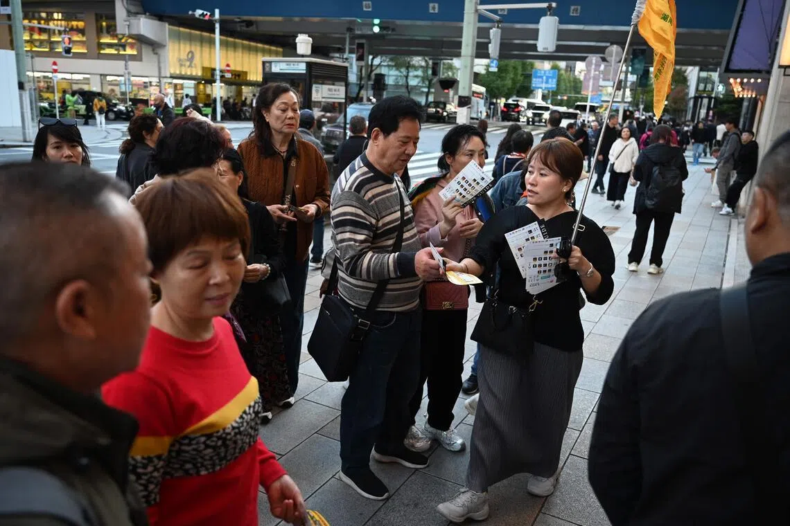A tour guide hands out leaflets for a popular duty-free store to members of a Chinese tour group in Tokyo.
