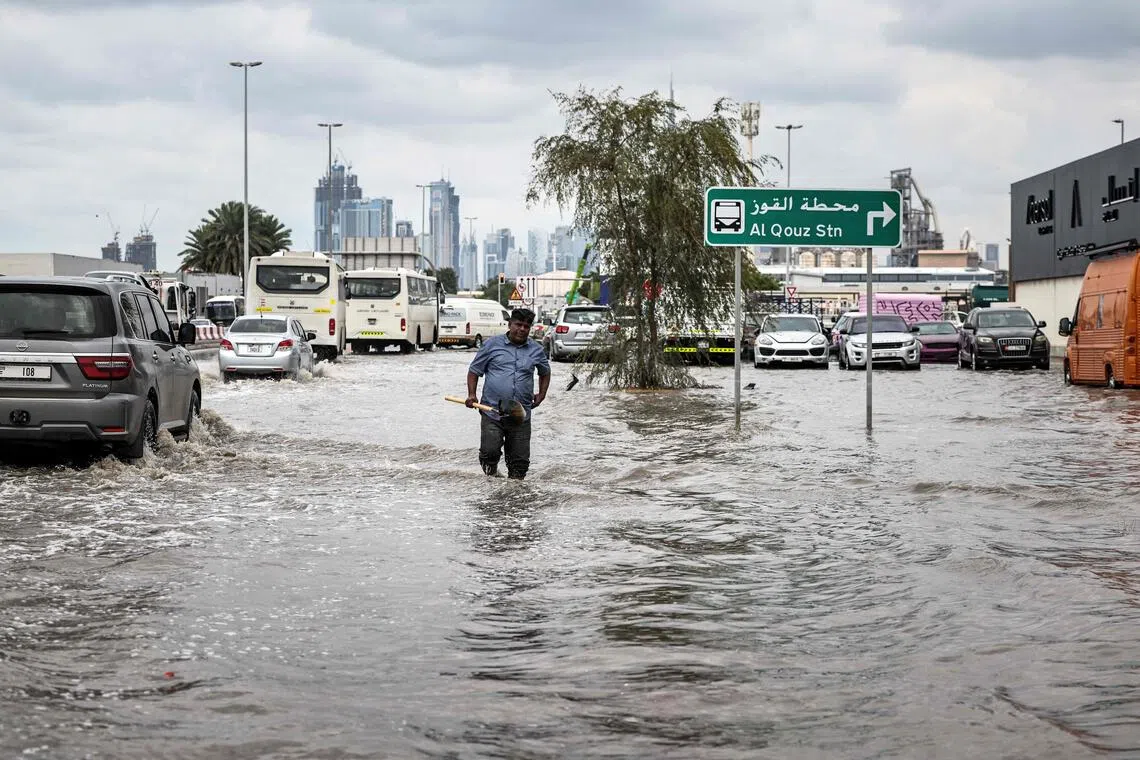 A man carries a spade to unblock a drain as he walks through floodwaters following heavy rains in Dubai.
