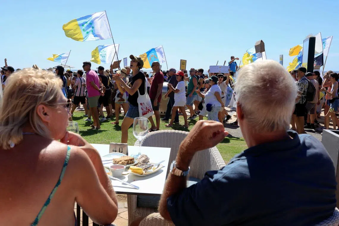 A couple of tourists sitting on a terrace watch a demonstration for a change in the tourism model in the Canary Islands on the island of Gran Canaria, Spain, October 20, 2024. REUTERS/Borja Suarez