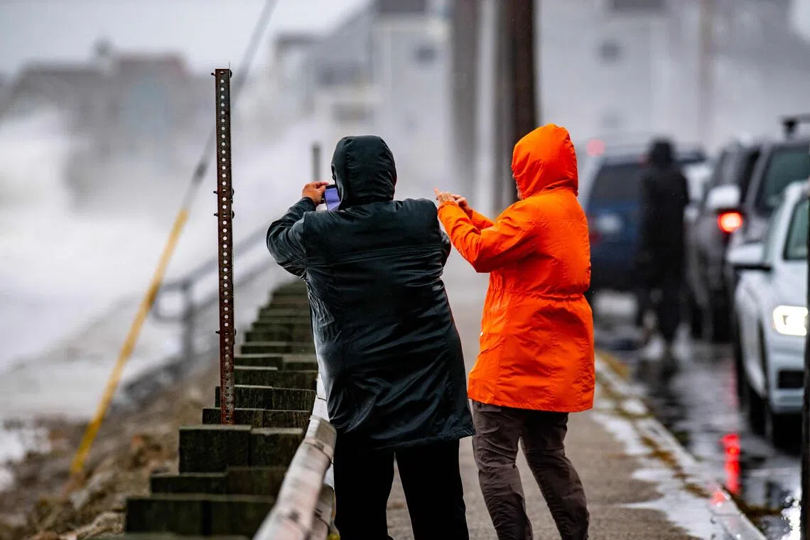 People taking photos on Sept 26 in Scituate, Massachusetts, as waves pound the shore.