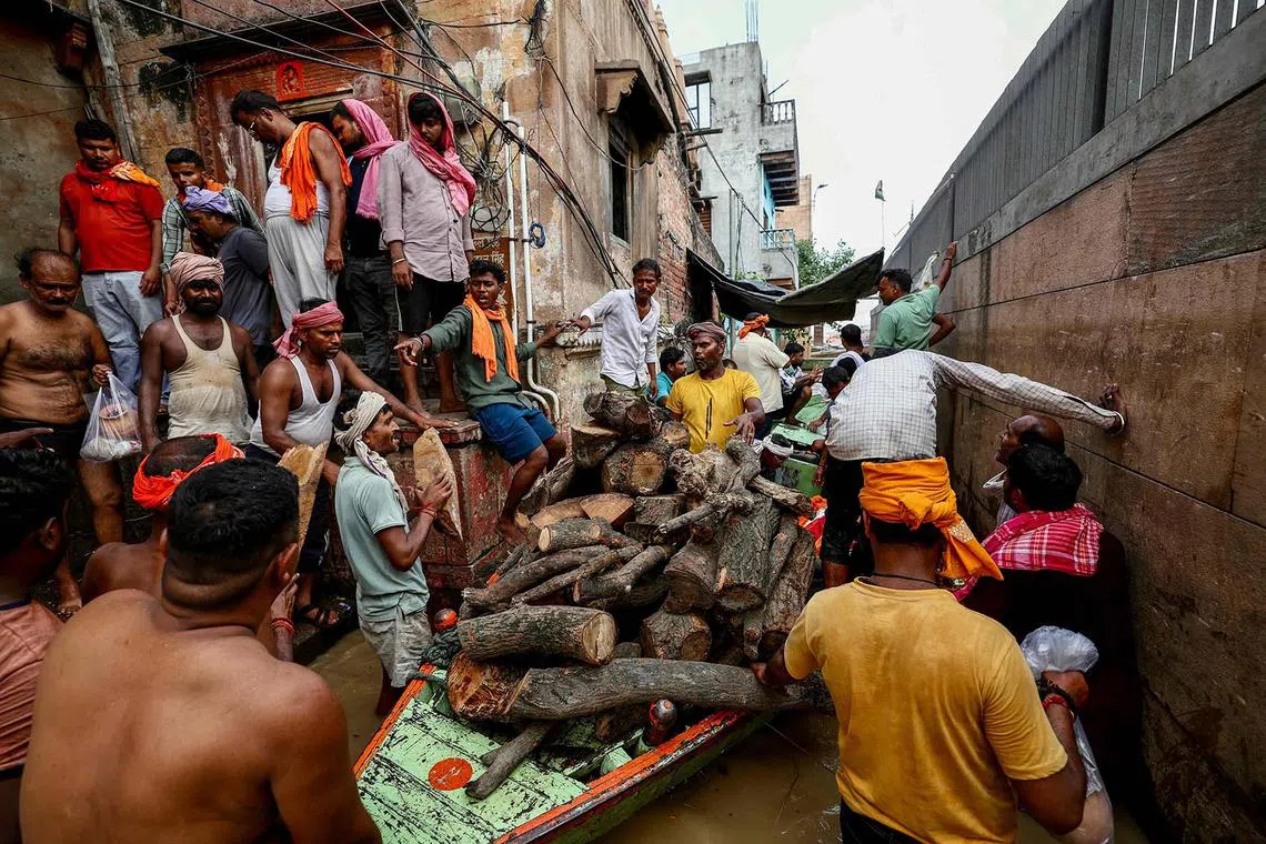 Workers transporting wood for funeral rites of a deceased in a flooded lane at the Manikarnika Ghat, after the water level of Ganges River rose on Aug 28, 2025. 
