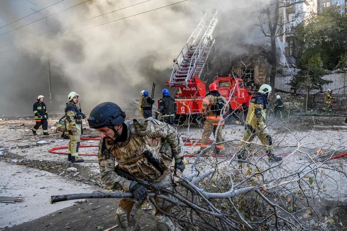 Firefighters help a local woman in Kyiv evacuate from a building destroyed by a Russian drone strike, on Oct 17, 2022. 