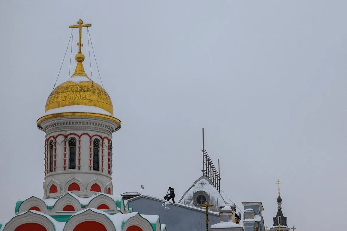 A worker removing snow from the roof of a building next to a church following a heavy snowfall in Moscow, Russia, Nov 27, 2023.