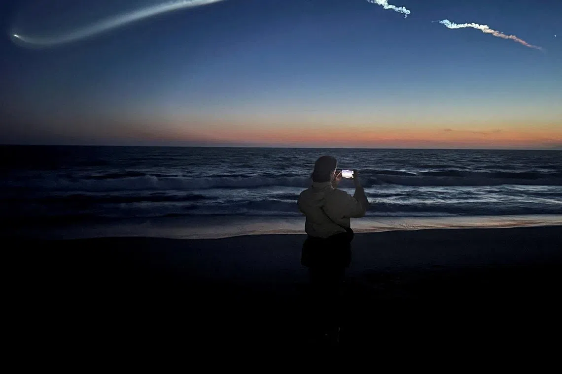 FILE PHOTO: A person takes photos of a trail as the Falcon 9 carrying Starlink satellites streaks across the sky in the latest SpaceX launch as viewed from Venice Beach in Los Angeles, California, U.S., April 6, 2026.   REUTERS/Daina Beth Solomon/File Photo