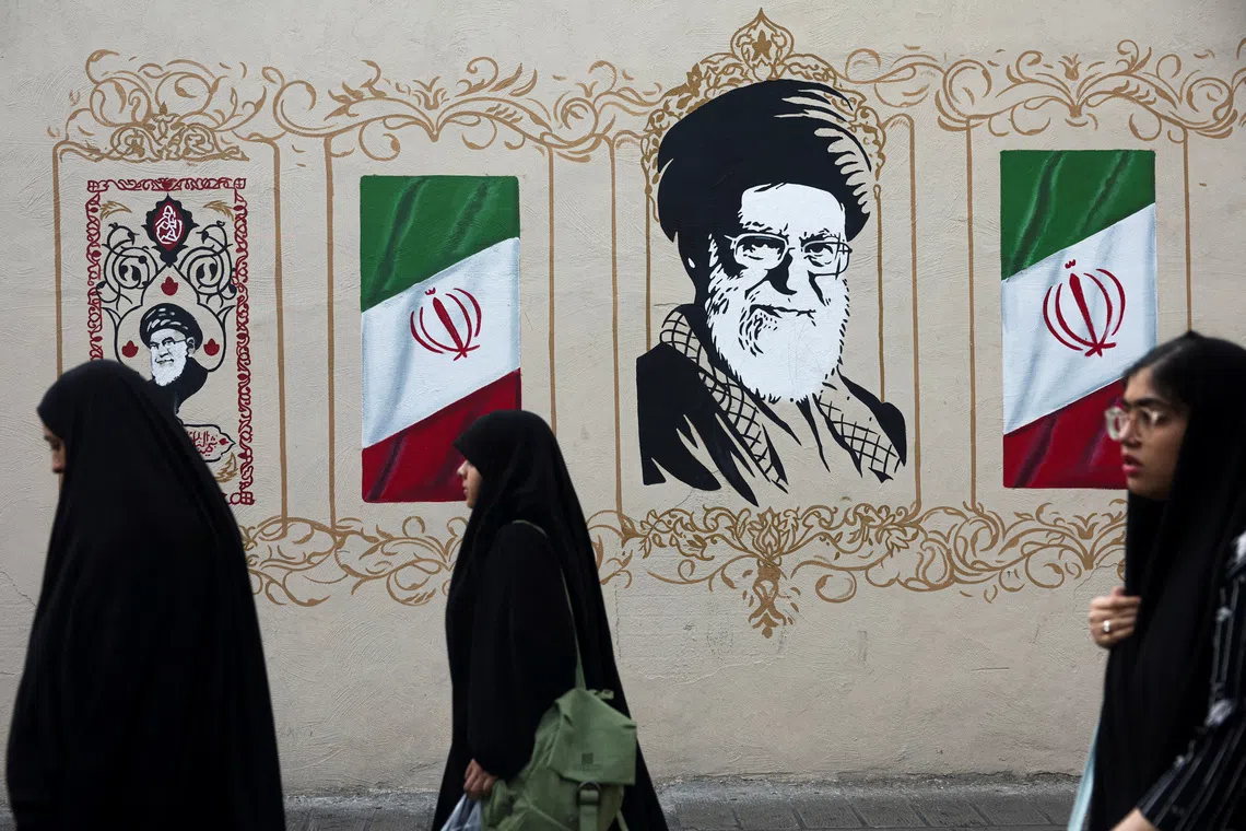 Mural of a man flanked by Iranian flags, with women in black standing in front.