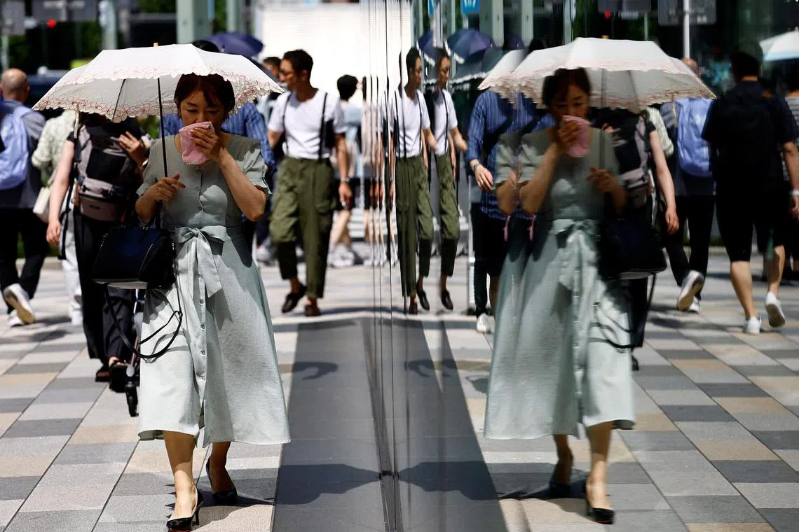 A passerby holding a parasol wipes her face as she walks on the street as the Japanese government issued a heatstroke alert in Tokyo and other prefectures, in Tokyo, Japan July 9, 2024. REUTERS/Issei Kato


