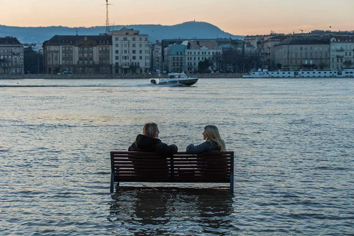 Women sitting on a bench surrounded by flood water of the River Danube in Budapest, Hungary, on Dec 28, 2023, as the lower quays of the riverbank are underwater due to flooding. 