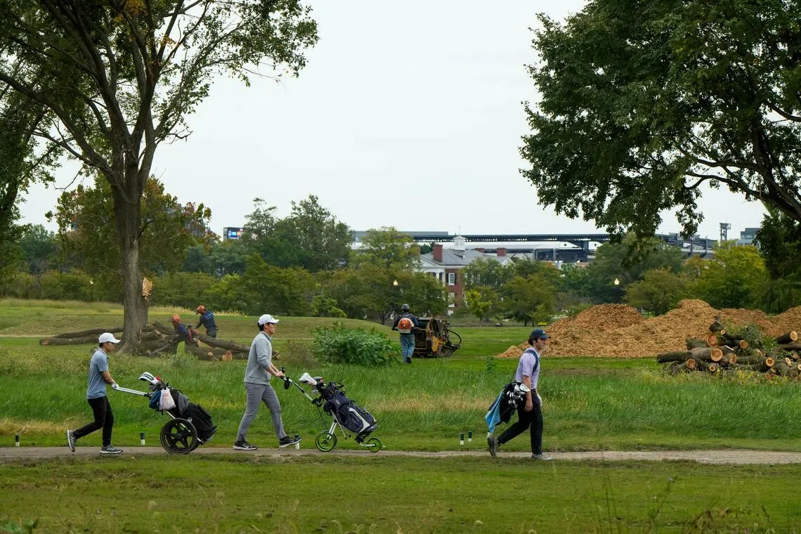 Golfers walk past workers removing trees at East Potomac Golf Links golf course in Washington, DC, on Oct 10.