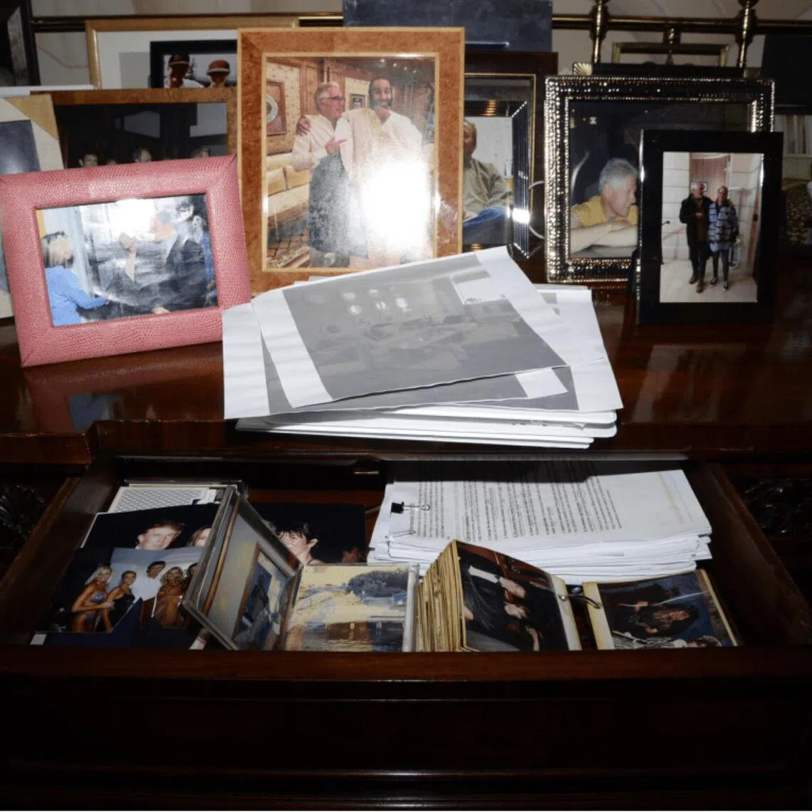 A credenza covered in photographs in a home of Jeffrey Epstein in an undated photo released by the US Department of Justice on Dec 19, 2025. More than a dozen photos, including one featuring President Donald Trump, were removed without explanation.
