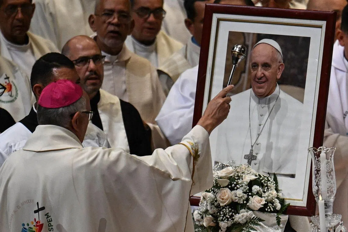 The Archbishop of the Archdiocese of Caracas, Raul Biord Castillo, sprinkles holy water on a portrait of the late Pope Francisco during a mass in his honor in Caracas on April 26, 2025. Pope Francis was buried Saturday in the Basilica of Santa Maria Maggiore in Rome, after a crowded farewell to the pontiff who came from the “end of the world” and who put the underprivileged at the heart of the Catholic Church. (Photo by Juan BARRETO / AFP)
