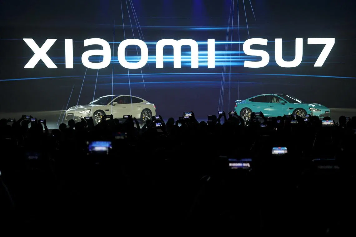 Attendees hold their mobile phones as Xiaomi unveils its first electric vehicle (EV) SU7 onstage, at an event in Beijing, China December 28, 2023. REUTERS/Florence Lo