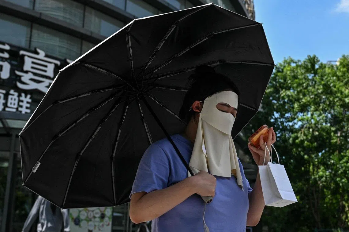 TOPSHOT - A woman protects herself from the sun with a umbrella and a face mask while walking on a street in Shanghai on July 15, 2026. (Photo by Hector RETAMAL / AFP)