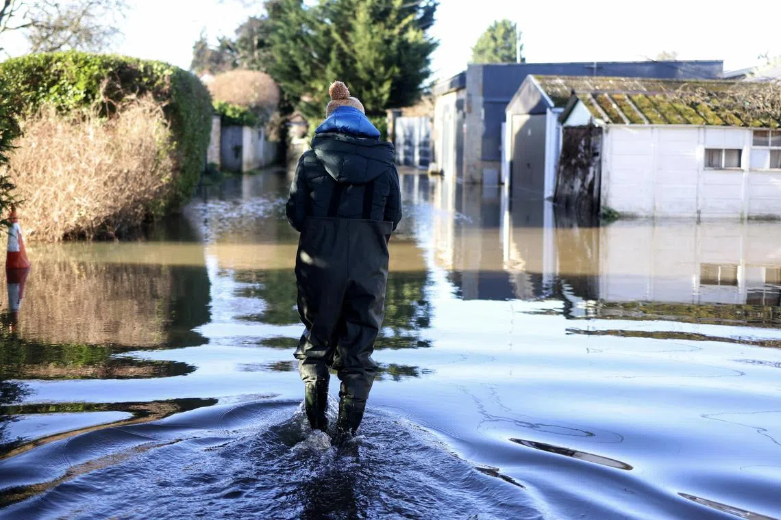 epa11067628 A person wades through flood water along a street in the flood-hit village of Wraysbury, south-west of London, Britain, 10 January 2024. Flood warnings remain in place following last week’s Storm Henk, which has led to mass flooding and travel disruptions in parts of south England and Midlands.  EPA-EFE/NEIL HALL