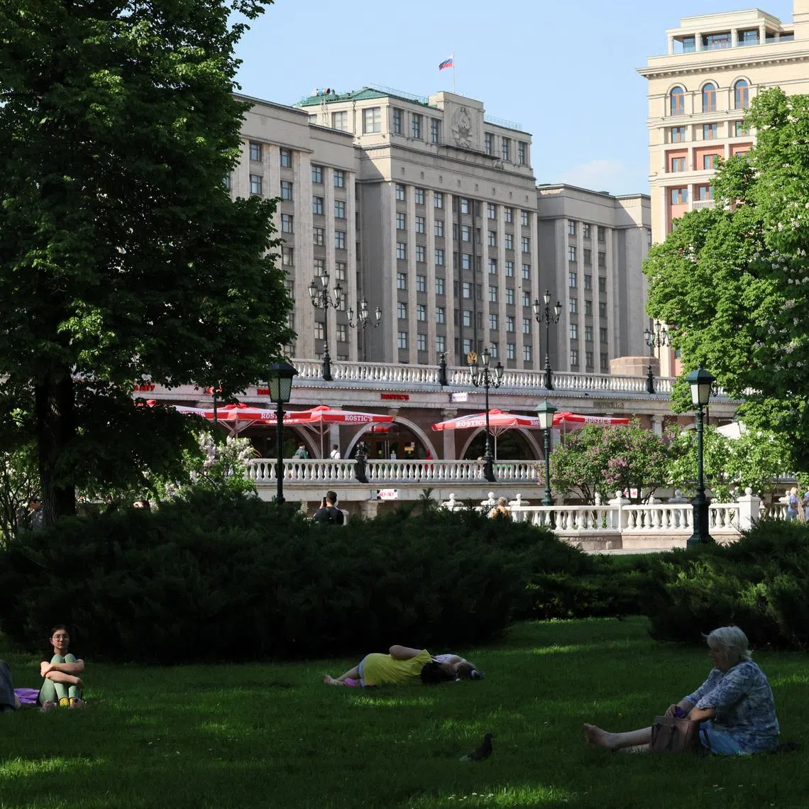 People relax on the grass in Alexander Garden, with the headquarters of the lower house of Russia’s parliament, the State Duma, seen in the background, on a hot spring day in central Moscow, Russia, May 19, 2026. REUTERS/Anastasia Barashkova