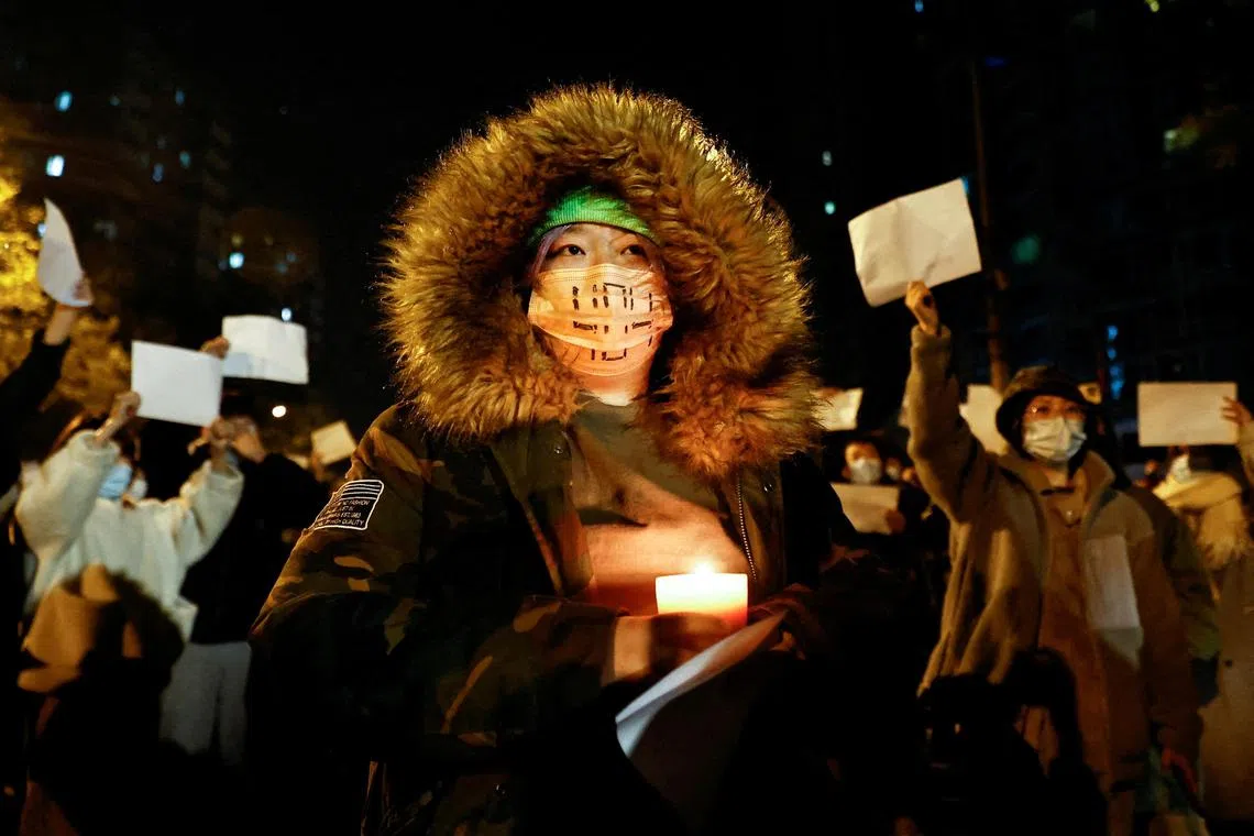 A person holds a candle, as people gather for a vigil and hold white sheets of paper in protest of Covid-19 restrictions, during a commemoration of the victims of a fire in Urumqi, as outbreaks of the coronavirus disease continue in Beijing, China, November 27, 2022. 