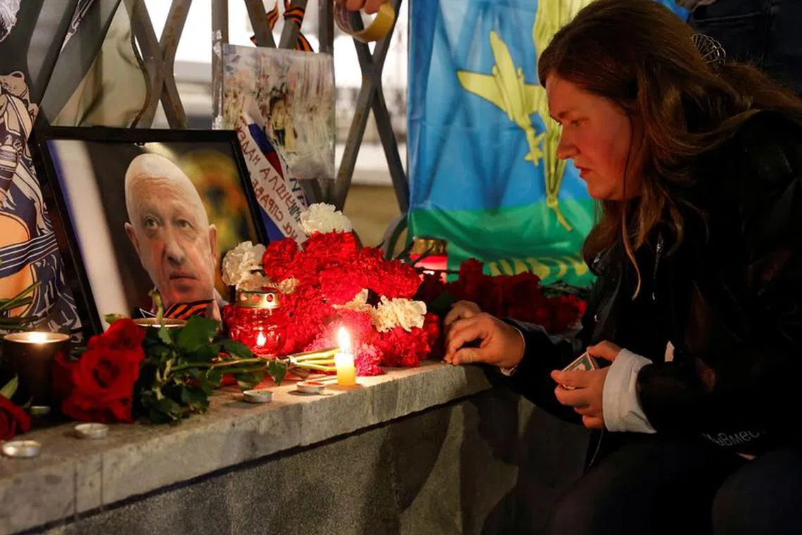 A woman lights a candle in front of a portrait of Wagner mercenary chief Yevgeny Prigozhin at a makeshift memorial in Moscow, Russia August 24, 2023. REUTERS/Stringer