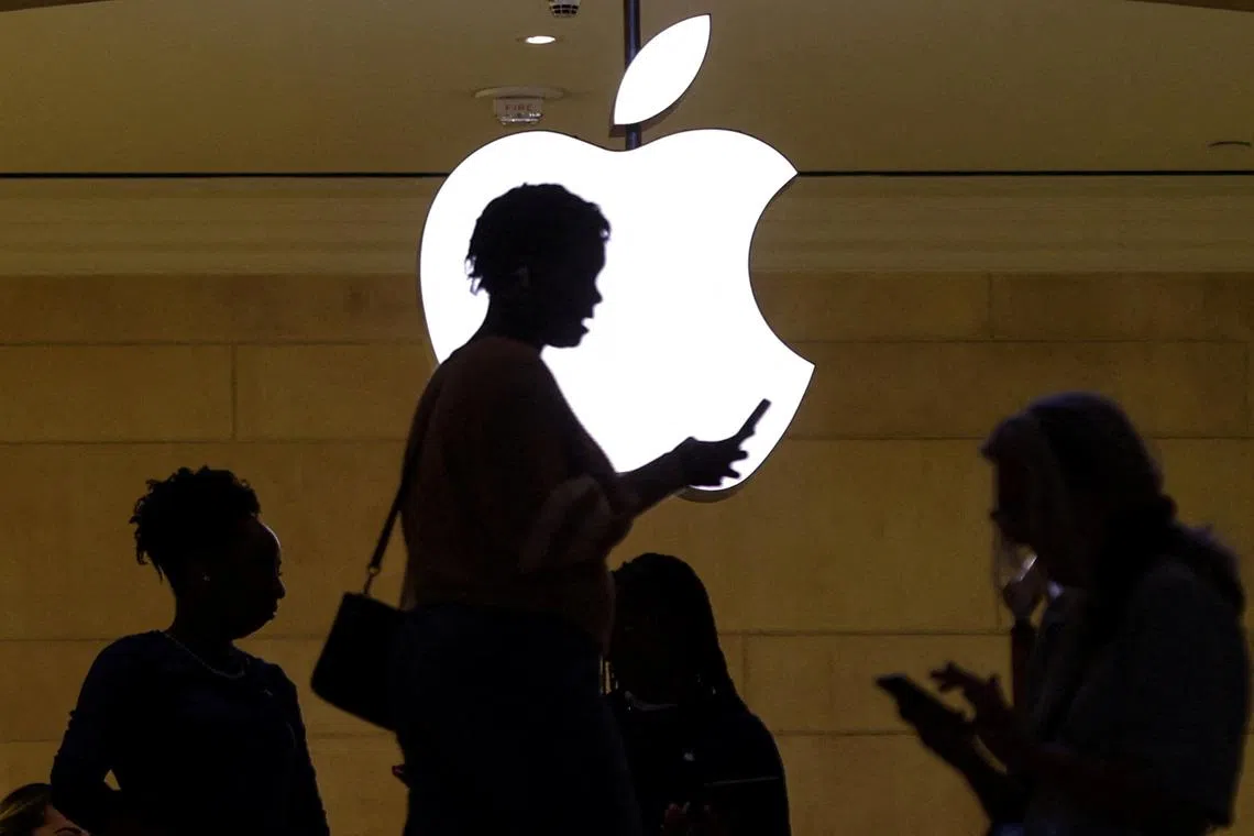 FILE PHOTO: A women uses an iPhone mobile device as she passes a lighted Apple logo at the Apple store at Grand Central Terminal in New York City, U.S., April 14, 2023. REUTERS/Mike Segar/File Photo
