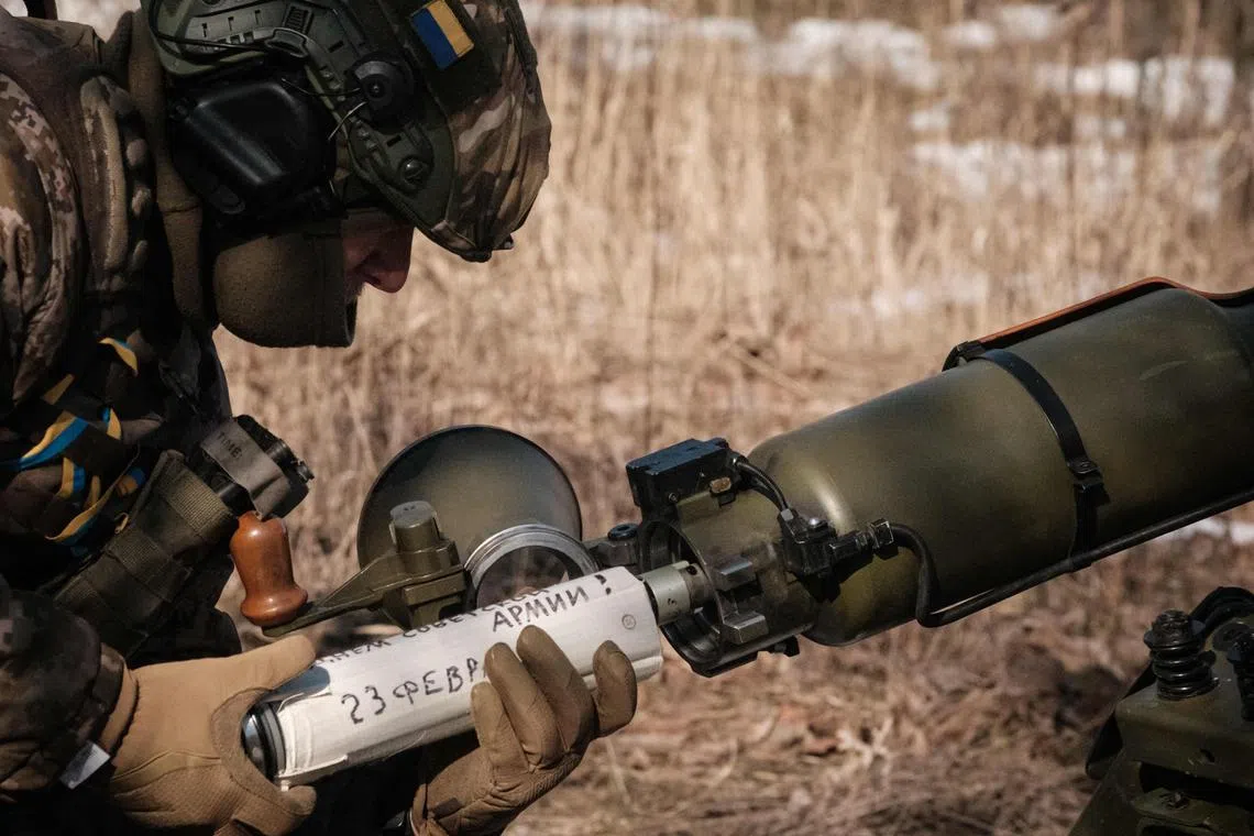 A Ukrainian serviceman prepares a shell near Bakhmut for firing towards Russian positions, featuring a message written in Ukrainian: "Happy Soviet Army Day, February 23".