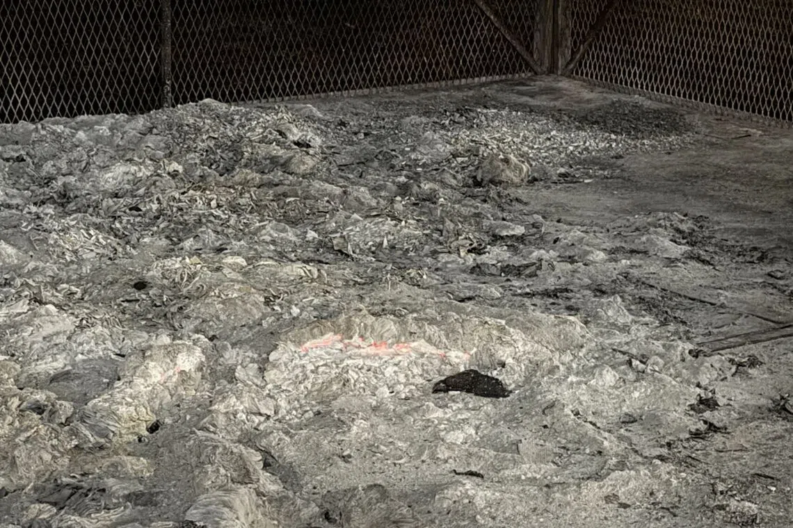 Glowing embers visible on burnt joss paper inside the metal cage.