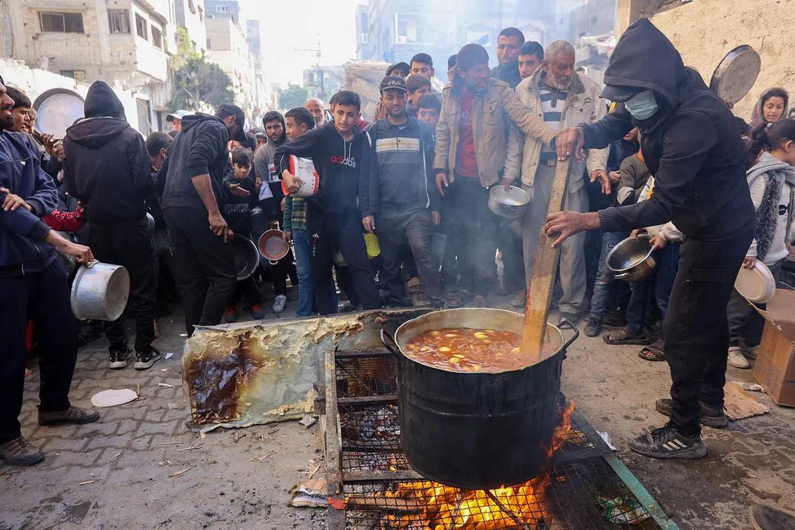 TOPSHOT - A volunteer stirs a food pot as Palestinians wait to collect humanitarian aid portions, in al-Shati camp near Gaza City on December 26, 2024, amid the ongoing war between Israel and the Palestinian Hamas movement. (Photo by Omar AL-QATTAA / AFP)