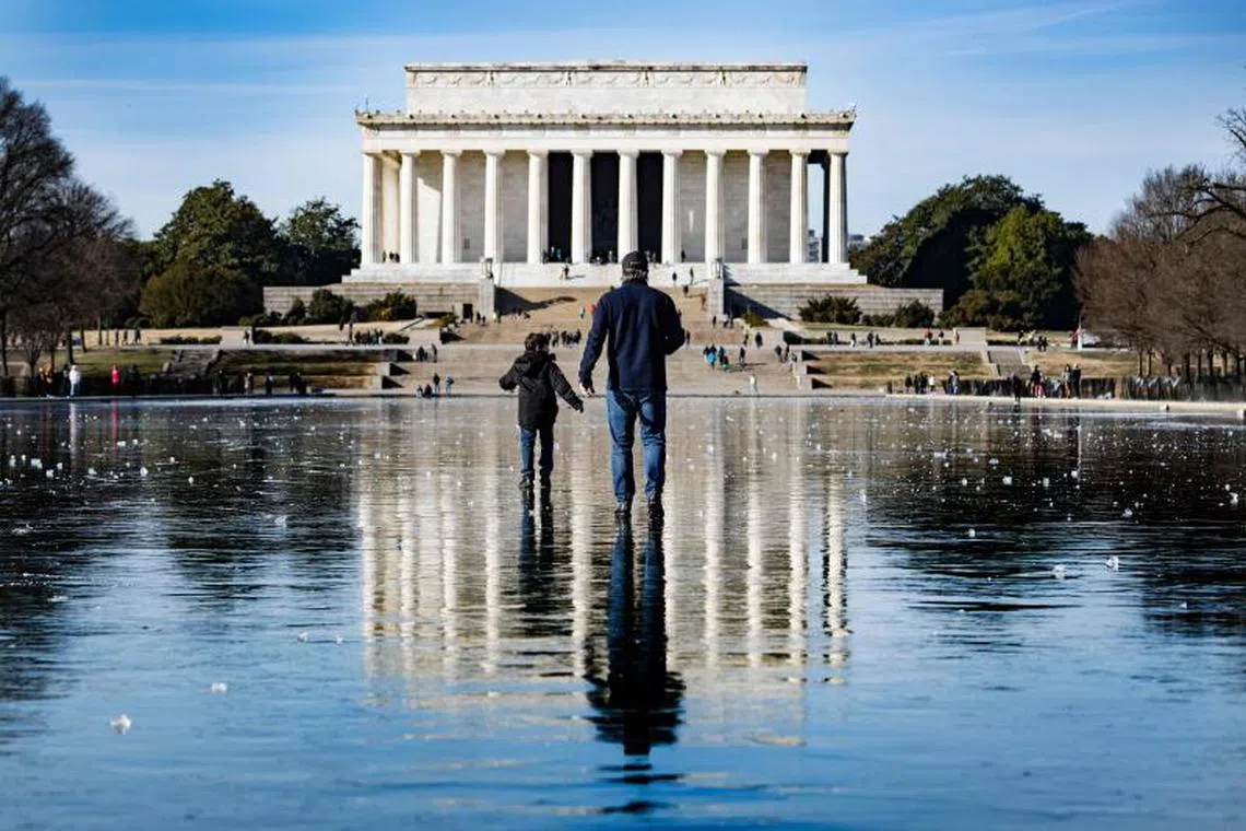 A man and a boy walk across the frozen Reflecting Pool towards the Lincoln Memorial on the National Mall in Washington, DC, on December 26, 2022. - Heavy snow, howling winds, and air so frigid it instantly turned boiling water into ice took hold of much of the US over Christmas weekend, including normally temperate southern states. PHOTO : AFP