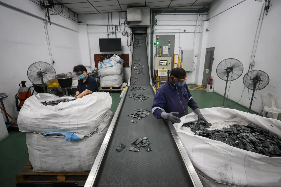 Workers placing loose mobile phone batteries onto a conveyor belt to be shredded at the TES Singapore battery recycling facility in Tuas, 30 Nov 2022.