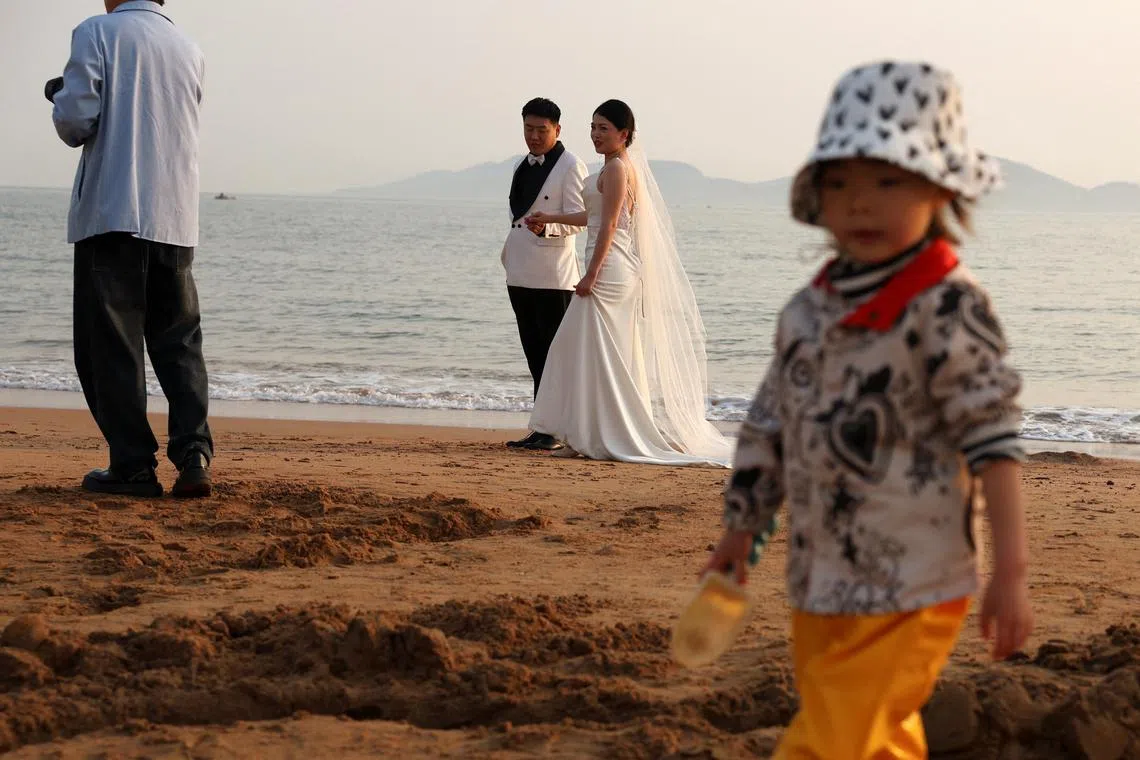 FILE PHOTO: A child plays with sand near a couple taking part in a pre-wedding photoshoot on a beach in Qingdao, Shandong province, China April 21, 2024. REUTERS/Florence Lo/File Photo