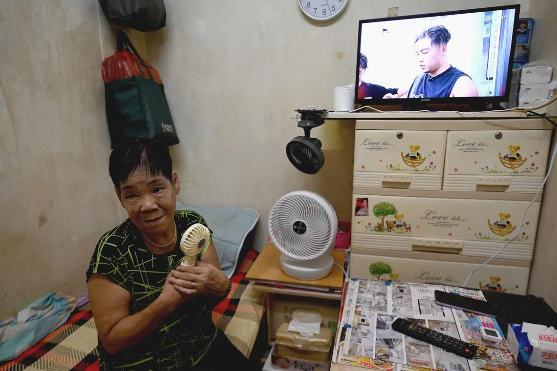 Retired janitor Chun Loi, 84, sits on her bed while facing electric fans inside her 50-square-foot windowless one-room flat in Hong Kong. 