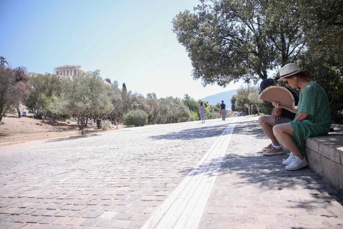 A tourist uses a fan to cool herself off in the shade near The Acropolis in Athens on July 12, 2024. 