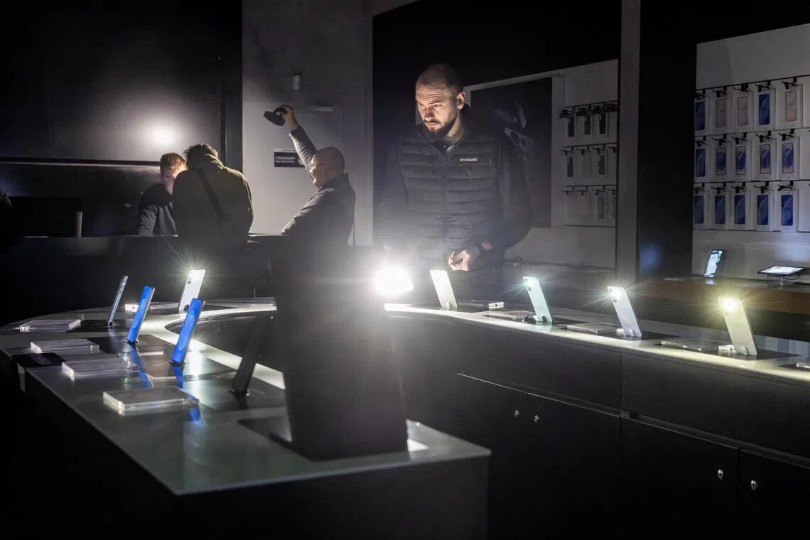 A shop assistant turning on the flashlights of smartphones at a mobile phone shop in Kharkiv, Ukraine, during the electricity blackout on Jan 31.