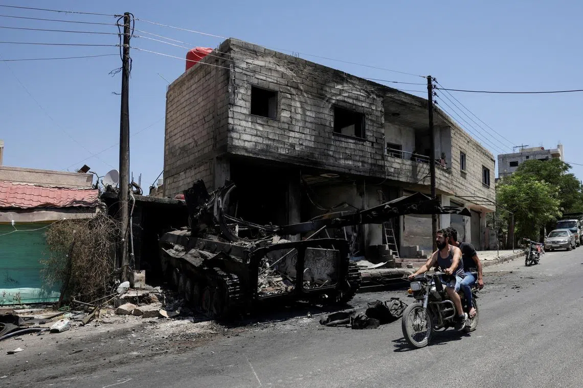 FILE PHOTO: People ride a motorcycle past a burned-out military vehicle, following deadly clashes between Druze fighters, Sunni Bedouin tribes and government forces, in Syria's predominantly Druze city of Sweida, Syria July 25, 2025. REUTERS/Khalil Ashawi/File Photo