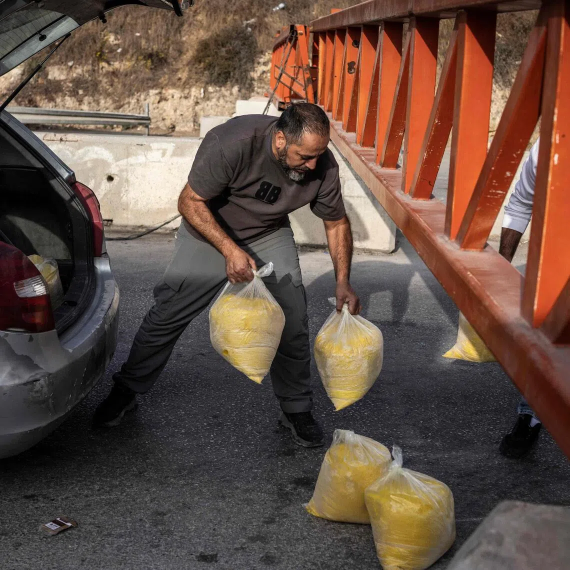 People pass packages under a closed checkpoint gate to the Israeli occupied West Bank city of Hebron on Oct 24.