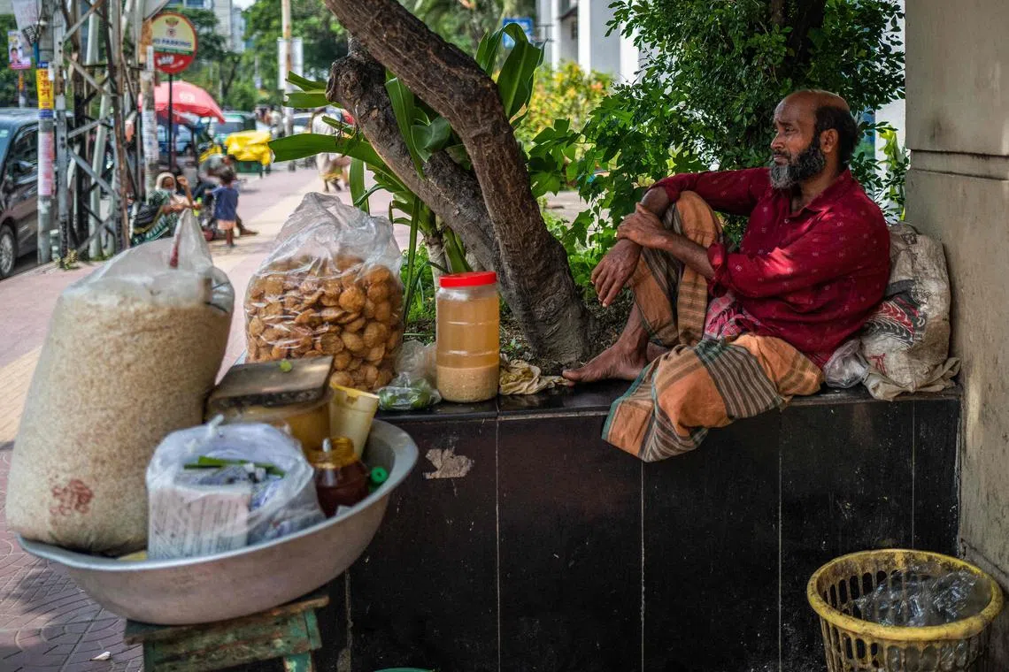 A vendor selling traditional snacks sits under the shade of a tree in Dhaka on Aug 26, 2022. (Photo by Jewel SAMAD / AFP)