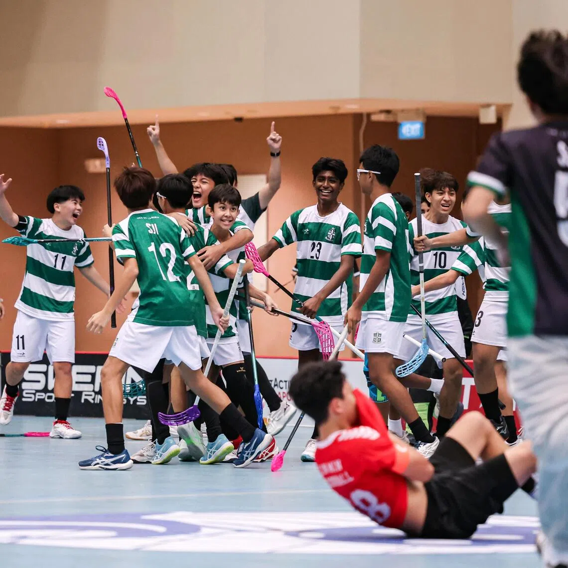 St Joseph’s Institution players celebrating after the final whistle as Xinmin Secondary School captain Firhan Hafiz lies on the floor in dejection during the National School Games C Division boys’ floorball final.