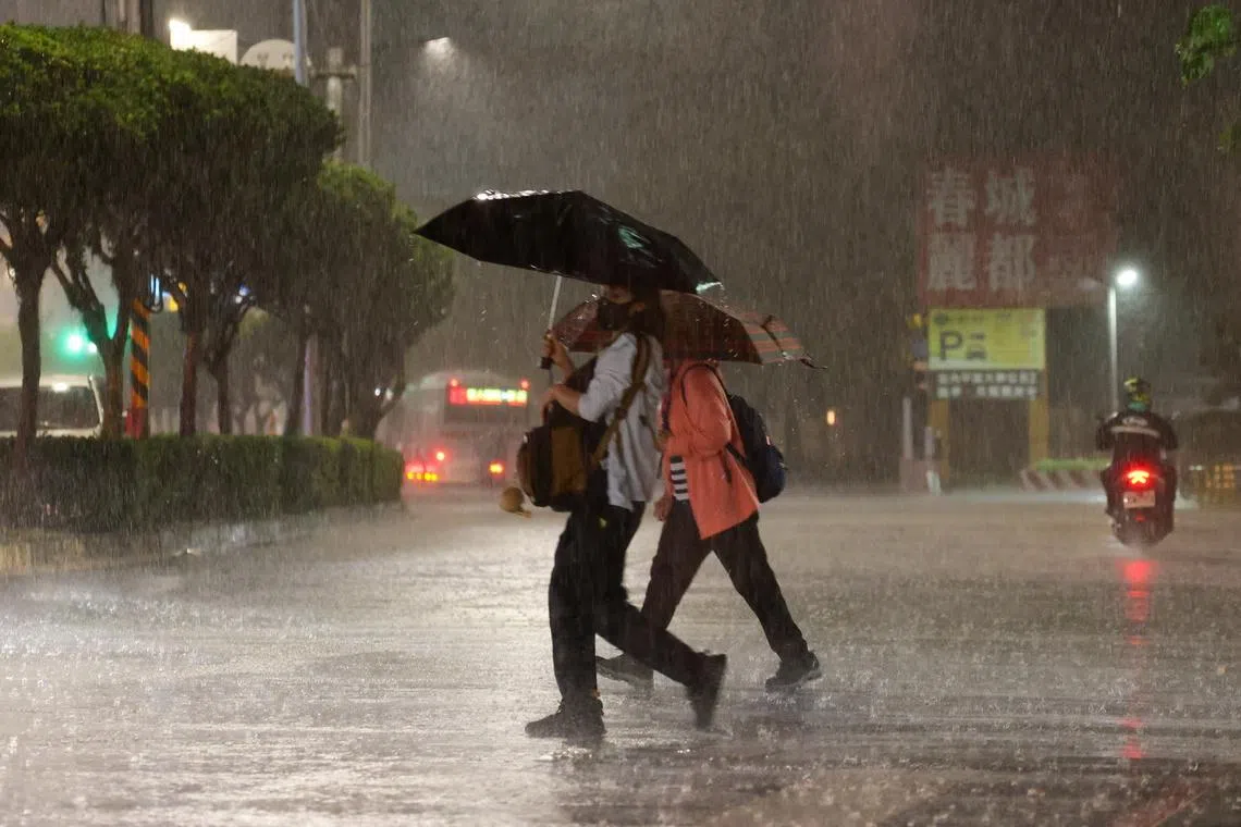 People walk across the street during a downpour of rain in Taipei, Taiwan, 25 June. Rainfall tied to Typhoon Mekkhala was expected, prompting officials to open shelters and step up monitoring of key roads and facilities.